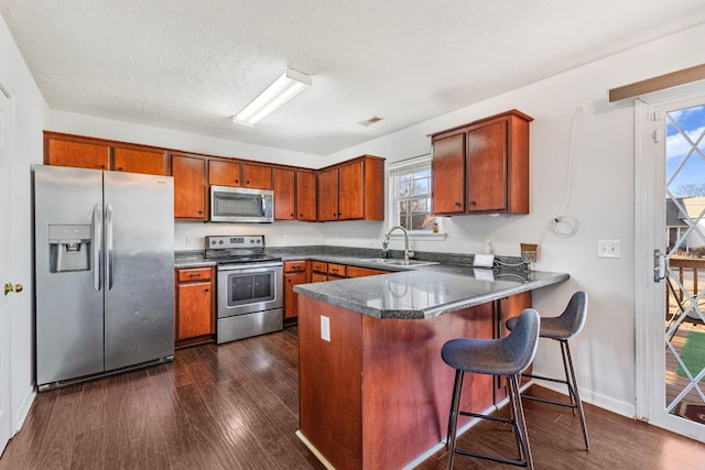 kitchen featuring sink, dark wood-type flooring, appliances with stainless steel finishes, a textured ceiling, and kitchen peninsula