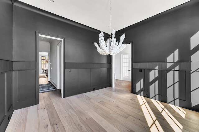 unfurnished dining area featuring an inviting chandelier and light hardwood / wood-style flooring