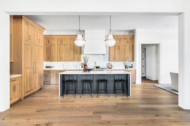 kitchen featuring pendant lighting, a kitchen bar, custom range hood, a center island with sink, and light wood-type flooring