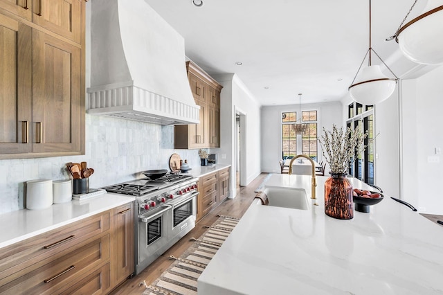 kitchen featuring pendant lighting, sink, backsplash, custom exhaust hood, and range with two ovens