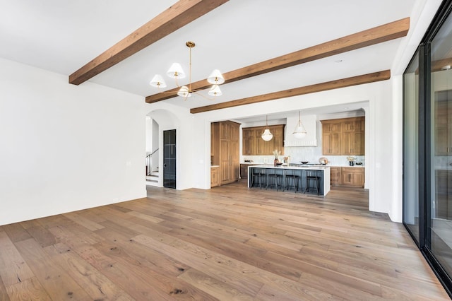 unfurnished living room featuring a notable chandelier, beam ceiling, and wood-type flooring