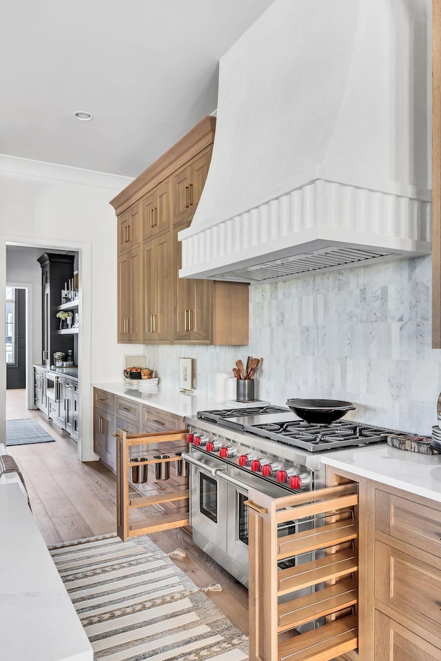 kitchen with premium range hood, tasteful backsplash, ornamental molding, light hardwood / wood-style floors, and range with two ovens