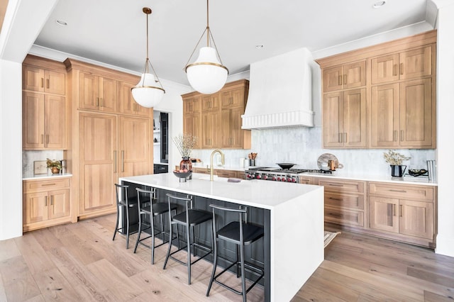 kitchen featuring a breakfast bar, sink, backsplash, a kitchen island with sink, and custom range hood