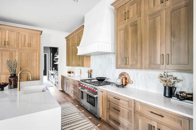 kitchen featuring sink, custom exhaust hood, light wood-type flooring, double oven range, and backsplash