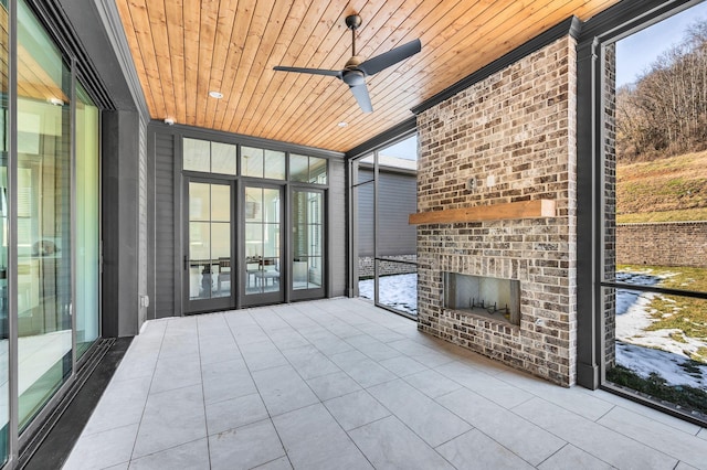 unfurnished sunroom featuring an outdoor brick fireplace, ceiling fan, a wealth of natural light, and wood ceiling