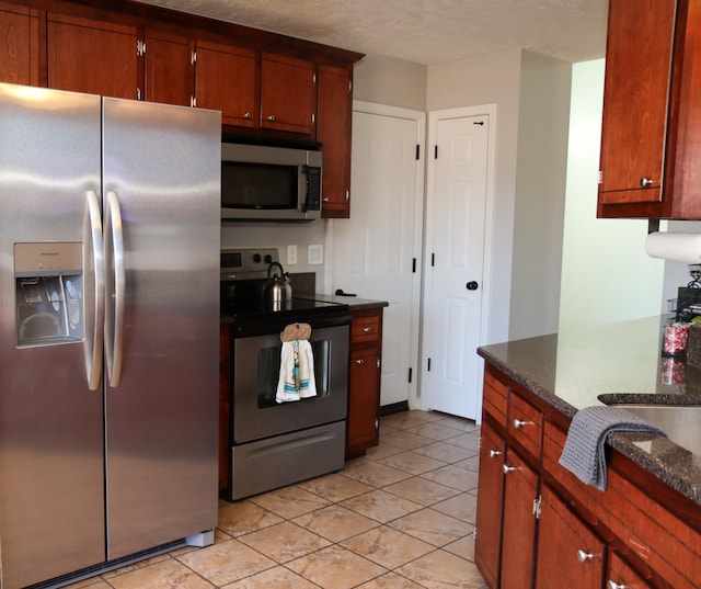 kitchen with appliances with stainless steel finishes, light tile patterned floors, and dark stone countertops