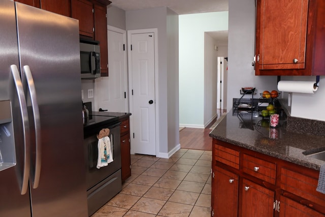 kitchen featuring appliances with stainless steel finishes, light tile patterned floors, and dark stone counters