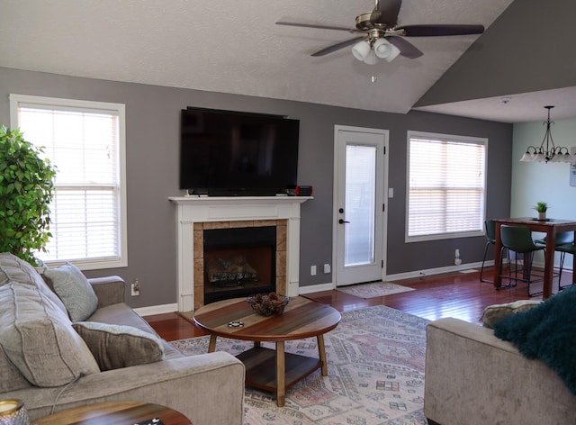 living room featuring vaulted ceiling, ceiling fan with notable chandelier, hardwood / wood-style floors, and a fireplace