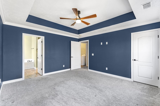 unfurnished bedroom featuring ensuite bath, ceiling fan, washer / dryer, light colored carpet, and a raised ceiling