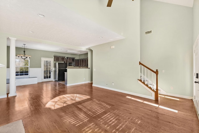 unfurnished living room featuring ceiling fan with notable chandelier, hardwood / wood-style floors, and decorative columns