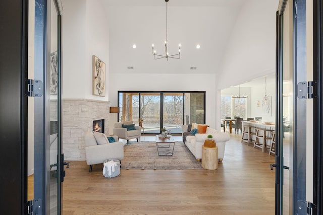 living room with a towering ceiling, a notable chandelier, a fireplace, and light hardwood / wood-style flooring