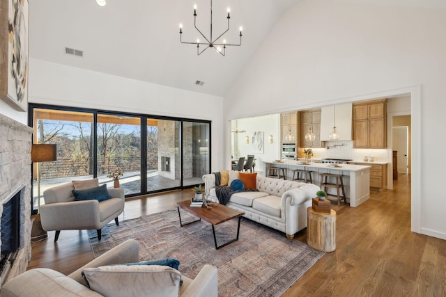 living room featuring wood-type flooring, a stone fireplace, a chandelier, and high vaulted ceiling