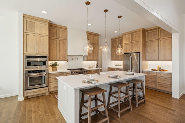 kitchen featuring a kitchen bar, wood-type flooring, a center island with sink, appliances with stainless steel finishes, and backsplash