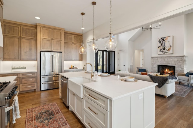 kitchen featuring sink, appliances with stainless steel finishes, hanging light fixtures, white cabinets, and a center island with sink