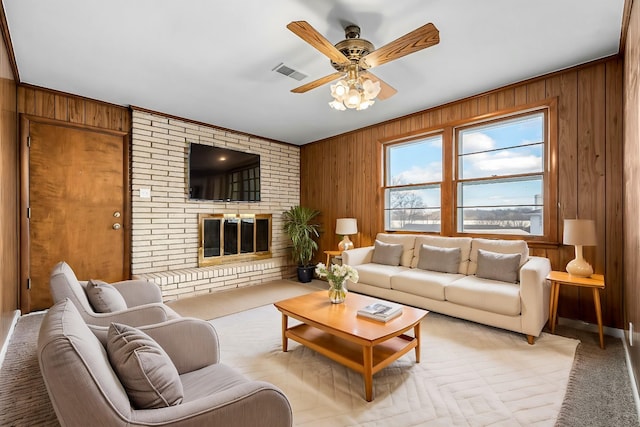 carpeted living room featuring ceiling fan, a fireplace, ornamental molding, and wooden walls