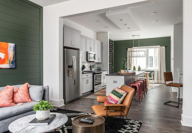 kitchen with a breakfast bar area, appliances with stainless steel finishes, dark hardwood / wood-style flooring, a kitchen island with sink, and white cabinets