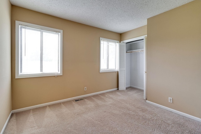 unfurnished bedroom featuring a closet, light carpet, and a textured ceiling