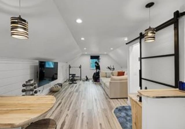 living room featuring lofted ceiling, a barn door, and light wood-type flooring