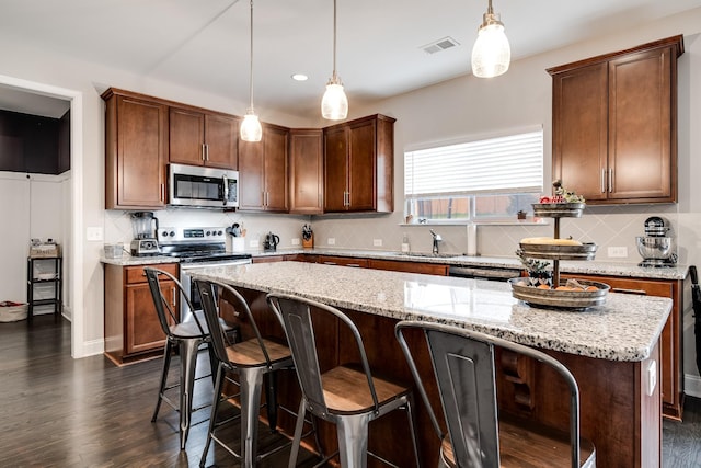 kitchen with light stone counters, stainless steel appliances, decorative light fixtures, and a center island