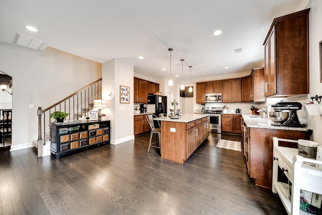 kitchen featuring a kitchen bar, hanging light fixtures, dark hardwood / wood-style flooring, a kitchen island, and stainless steel appliances