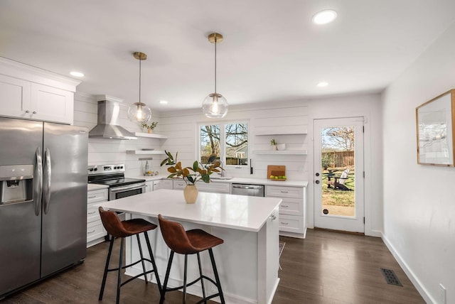 kitchen featuring white cabinetry, wall chimney range hood, decorative light fixtures, and stainless steel appliances