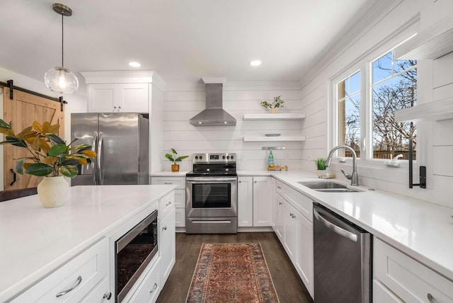 kitchen featuring pendant lighting, wall chimney range hood, sink, stainless steel appliances, and white cabinets