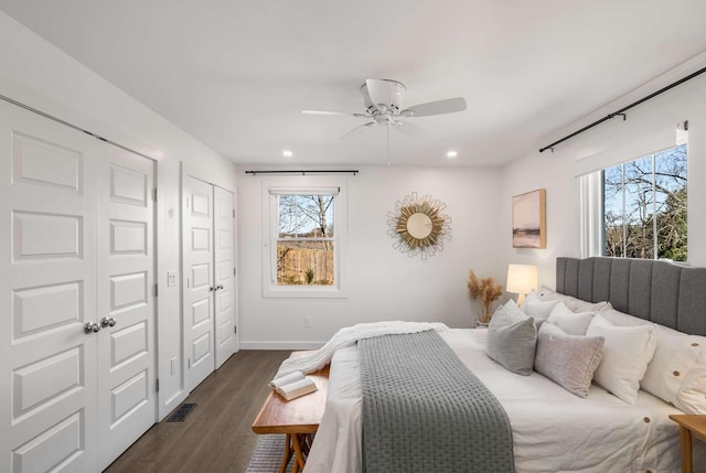 bedroom with dark wood-type flooring, ceiling fan, and two closets