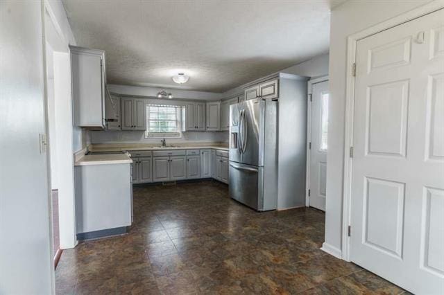 kitchen featuring stainless steel refrigerator with ice dispenser, sink, and gray cabinetry