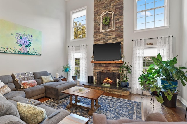 living room featuring a high ceiling, a stone fireplace, and hardwood / wood-style floors