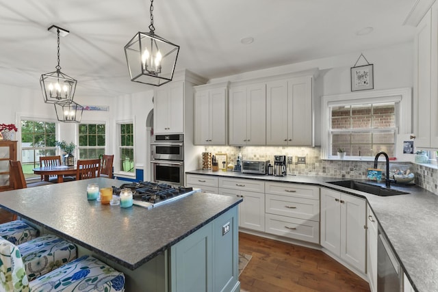 kitchen featuring appliances with stainless steel finishes, decorative light fixtures, sink, white cabinets, and a center island