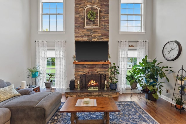 living room featuring a stone fireplace, hardwood / wood-style floors, a high ceiling, and a wealth of natural light