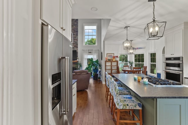 kitchen featuring pendant lighting, dark wood-type flooring, stainless steel appliances, white cabinets, and a kitchen bar