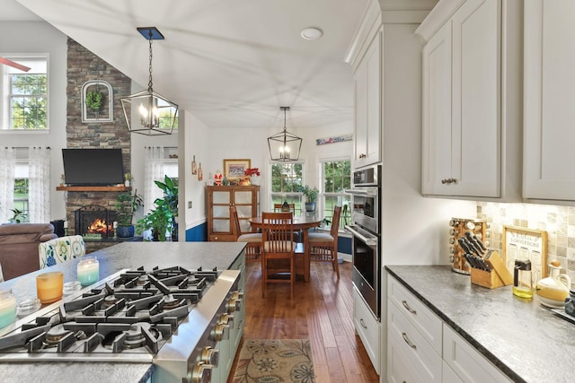 kitchen with hanging light fixtures, a stone fireplace, and white cabinets