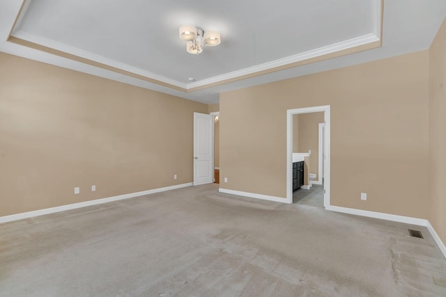 empty room with crown molding, light colored carpet, and a tray ceiling