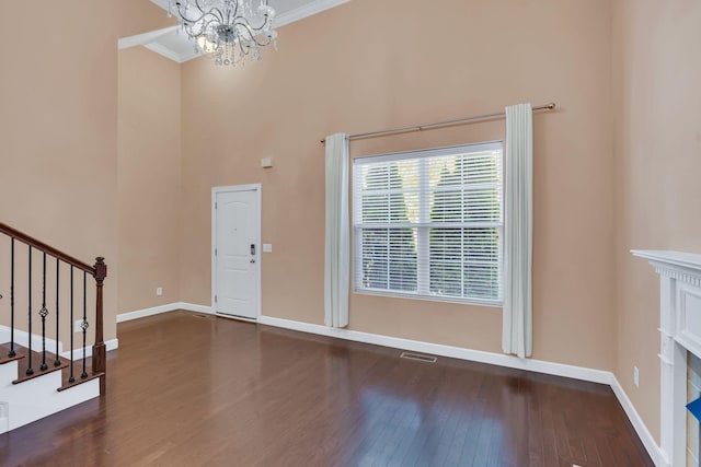 foyer with dark wood-type flooring, ornamental molding, a chandelier, and a high end fireplace