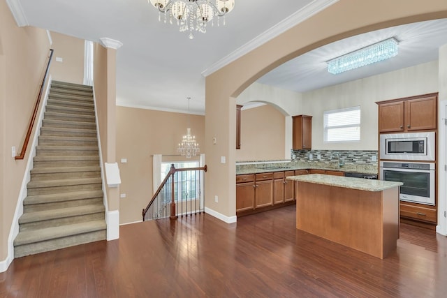 kitchen featuring appliances with stainless steel finishes, pendant lighting, decorative backsplash, a center island, and a notable chandelier