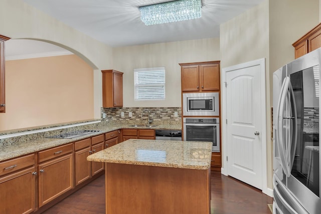 kitchen featuring sink, decorative backsplash, a center island, light stone counters, and stainless steel appliances