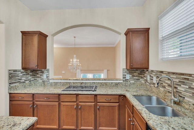 kitchen with sink, light stone counters, decorative light fixtures, black electric stovetop, and backsplash