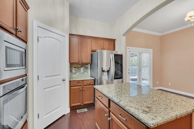 kitchen featuring tasteful backsplash, a center island, appliances with stainless steel finishes, dark hardwood / wood-style flooring, and light stone countertops