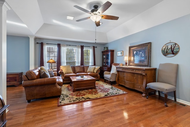 living room with a ceiling fan, a tray ceiling, ornate columns, and wood finished floors