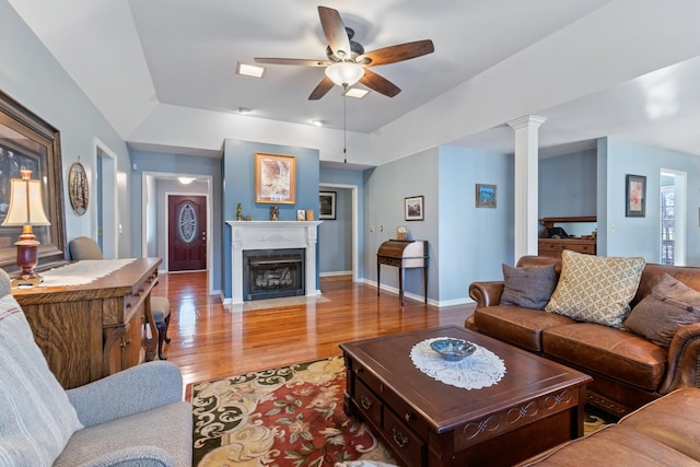 living room with decorative columns, baseboards, a fireplace with flush hearth, ceiling fan, and wood finished floors