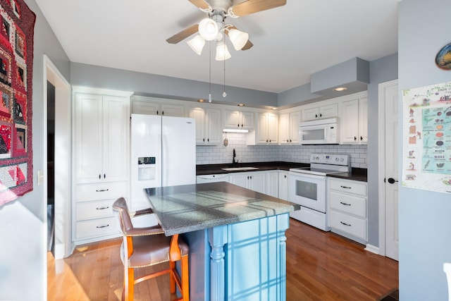 kitchen with white appliances, dark countertops, wood finished floors, white cabinetry, and a sink