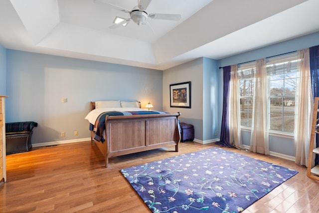 bedroom with ceiling fan, a tray ceiling, wood finished floors, and baseboards