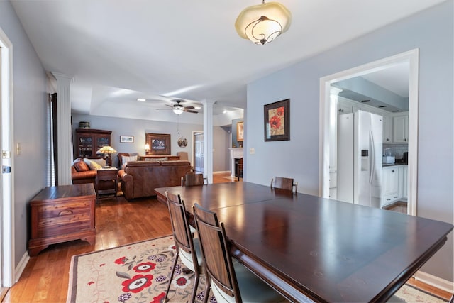 dining room featuring a ceiling fan, baseboards, ornate columns, and wood finished floors