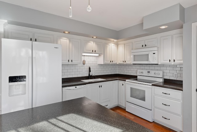 kitchen featuring dark countertops, white appliances, white cabinets, and a sink