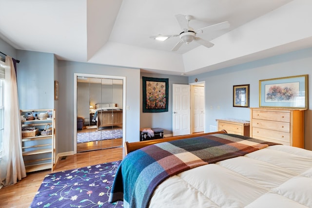 bedroom with light wood-type flooring, ceiling fan, a tray ceiling, and two closets