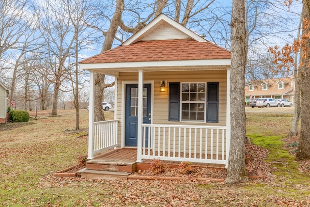 shotgun-style home featuring covered porch and a shingled roof