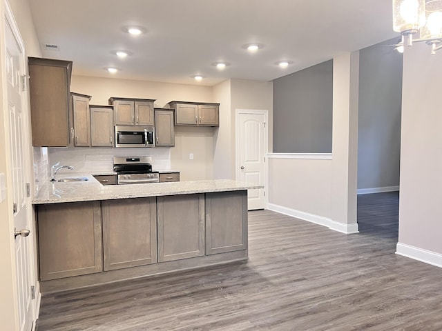 kitchen with sink, dark wood-type flooring, appliances with stainless steel finishes, light stone counters, and kitchen peninsula