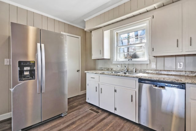 kitchen featuring white cabinets, appliances with stainless steel finishes, ornamental molding, dark wood-type flooring, and a sink