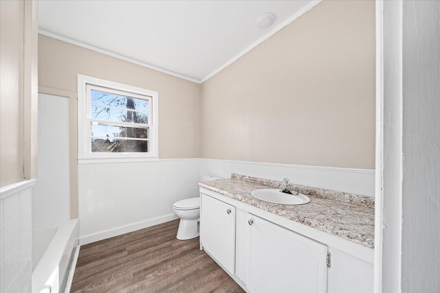 bathroom with toilet, a wainscoted wall, wood finished floors, vanity, and a tub